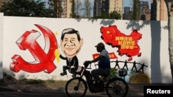 资料照:一名男子骑车路过北京街头一面印有习近平画像的宣传画。(2018年9月28日)