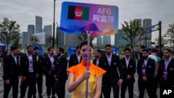 在中国杭州举行的第19届亚运会欢迎仪式上,一名志愿者举牌站在阿富汗塔利班政权派出的全部为男性运动员的队伍前。(2023年9月20日)