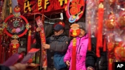 人们在北京街边小摊上购买对联等年货。(2024年2月9日)