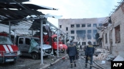 乌克兰救援人员走过乌东城市第聂伯河(Dnipro)一座被摧毁的救火站,救火站里停着几辆烧毁的紧急救援车辆。照片时间是2023年5月22号。