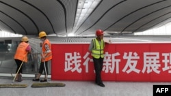 资料照:北京大兴国际机场的工人在一幅“践行新发展理论”的标语旁工作。(2019年7月9日)