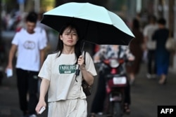 一名女子打着遮阳伞在酷暑中的武汉街头行走。(2024年8月1日)