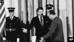 资料照片:1984年1月12日,时任美国总统里根在白宫西厅向时任中国总理赵紫阳示意在签署美中科技协议之前就座。(美联社照片)