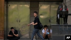 北京一家商场外的一头铜牛和路过的行人与看手机的工人。(2023年5月15日)