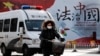 资料照:一辆警车和一名女子骑车驶过北京街头一堵宣传中国法治的宣传墙。(2016年12月28日)