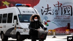 资料照:一辆警车和一名女子骑车驶过北京街头一堵宣传中国法治的宣传墙。(2016年12月28日)