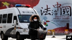 资料照:一辆警车和一名女子骑车驶过北京街头一堵宣传中国法治的宣传墙。(2016年12月28日)