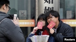 一对年轻人在北京一处婚姻登记处外手举结婚证留影。(2017年2月14日)