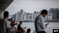 Orang-orang duduk di sepanjang kawasan pejalan kaki di sebelah pelabuhan Victoria di Hong Kong pada 31 Agustus 2023, sehari sebelum datangnya Topan Saola. (ISAAC LAWRENCE / AFP)