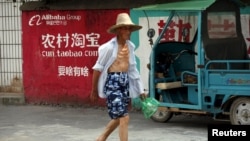 资料照:中国浙江桐庐一位农民走过淘宝的广告墙。(2015年7月20日)