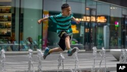 一个男孩在北京街头的喷水池玩水。(2023年7月1日)
