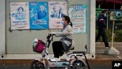 北京街头一名女子骑车路过墙上张贴的预防新冠病毒宣传画。(2022年10月26日)