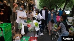 2022年4月25日,新冠肺炎疫情爆发后,戴着防护口罩的人们在商店外的摊位上购买蔬菜。