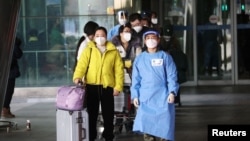 一名身穿防护外套的韩国军人2023年1月4日领着一批刚抵达仁川机场的中国旅客前往机场检疫中心。(路透社)