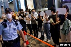 香港市民手持白纸和花束悼念新疆火灾死难者,支持中国内地的抗议活动。香港警察前去查看他们的身份证。(2022年11月28日)
