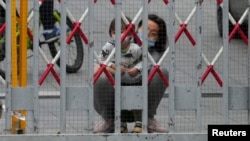 上海封城,一名女子和一个幼童从被封闭的居民小区栅栏后向外张望。(2022年5月10日)