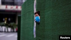 一位上海居民从封闭小区的围栏空隙中伸出头来张望。(2022年5月6日)