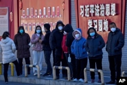 北京市民在宣传习近平思想的标语墙前排队等候接受核酸检测。(2022年12月5日)