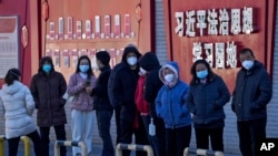 北京市民在宣传习近平思想的标语墙前排队等候接受核酸检测。(2022年12月5日)