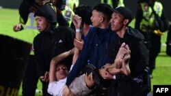 在这张2022年10月1日的照片中,在东爪哇马郎市的坎朱鲁汗体育场,阿雷马足球俱乐部和帕尔斯巴亚的足球比赛结束后发生踩踏事件,一群人抬着一名受伤的男子。