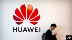 一名男子站在中国科技公司华为的广告牌旁使用智能手机(2019年10月31日)。