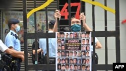 资料照片:2021年9月19日,香港一名抗议者站在模拟监狱铁窗后面,手里拿着根据《国家安全法》受审的民主派人士的照片。(法新社照片)