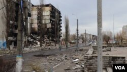 2022年4月6日,在基辅郊区城镇博罗江卡,少数居民骑着自行车经过被摧毁的楼群。(美国之音希瑟·默多克拍摄)