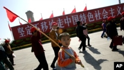 资料照:一个男孩手举红旗走过天安门广场上竖立的走中国特色社会主义道路的标语牌。(2007年10月9日)