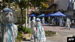 身穿防护服的工作人员在上海静安区的一个测试点看着居民做新冠病毒测试。(2022年4月4日)
