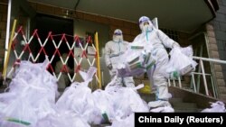 身穿防护服的工作人员给北京朝阳区一个被封控的居民楼发放新冠核酸检测盒。(2022年11月21日)