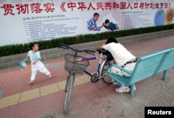 资料照:北京街道上一名小女孩在宣传中国人口与计划生育法的宣传栏下玩耍。