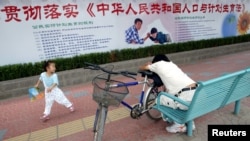 资料照:北京街道上一名小女孩在宣传中国人口与计划生育法的宣传栏下玩耍。