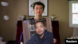 资料照片:中国维权律师丁家喜的妻子罗胜春在纽约家中手举着丈夫的照片。(2022年7月28日)