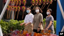 在中国北京街头戴着口罩的妇女经过一个摆放风车玩具的摊位(2022年9月13日)。