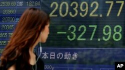 一位女士走过东京一家证券公司显示显示日经指数下跌的电子屏幕。(2015年8月12日)