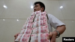 中国山西太原一家银行职员手捧成捆的人民币百元现钞。(资料照片)
