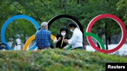 路人在坐落在日本奥委会总部附近的奥运五环徽标前闲谈。(路透社2021年6月23日照片)