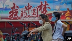 骑着电动车的中国女子驶过中国梦的宣传画。(2022年6月20日)