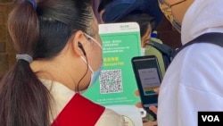 一名香港市民(白衣者)正准备使用防疫手机应用程式“安心出行”进入一间餐厅用膳,身旁的餐厅职员检视使用者是否有准确扫瞄餐厅入口的二维码 (美国之音/汤惠芸)