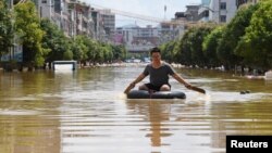 中国广东英德洪水泛滥的街头,一名男子划着一个轮胎过街。(2022年6月23日)