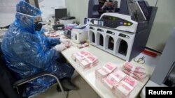 山西省太原市一名银行工作人员身穿雨衣戴着护眼镜和口罩点数人民币。(2020年2月24日)