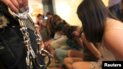 在浙江省温州市,一名警察提着手铐站在一群在“扫黄”行动中被抓捕的性工作者前。(2012年9月12日资料照)