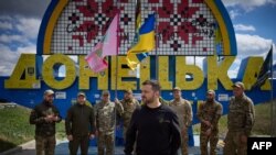 Rais wa Ukraine Volodymyr Zelensky akiwa na wanajeshi wa Ukraine mbele ya ishara ya barabara inayoashiria lango la eneo la Donetsk, katikati ya Russia. (Ofisi ya rais wa Ukraine / AFP).