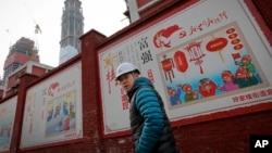 资料照:建筑工人走过北京一个居民小区外面,墙上有宣传牌《社会主义核心价值观:富强》《社会主义核心价值观:民主》(2016年12月13日)