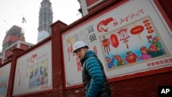 建筑工人走过北京一个居民小区外面,墙上有宣传牌《社会主义核心价值观:富强》《社会主义核心价值观:民主》(2016年12月13日)