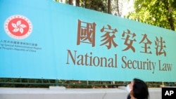 资料照:一名妇女走过香港街头宣传港版国安法的广告牌。(2020年6月30日)