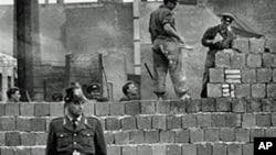 1961年10月7日,一名西柏林卫兵站在分隔东西柏林的混凝土墙前,同时,东德工人在为这道墙添砖加高。(资料照片)