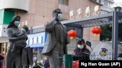 资料照片:在中国武汉市,一名女子正走过带着口罩的雕塑面前。世卫组织新冠溯源专家小组当时正在武汉考察。(2021年1月29日)