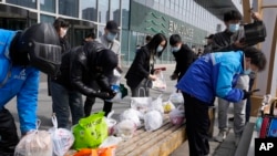 北京街头的快递小哥把消费者购买的食品放在居民楼外的长椅上。(2022年3月16日)
