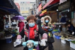 一名戴着口罩的妇女骑着电动车穿过武汉市的一个市场。(2020年1月24日)